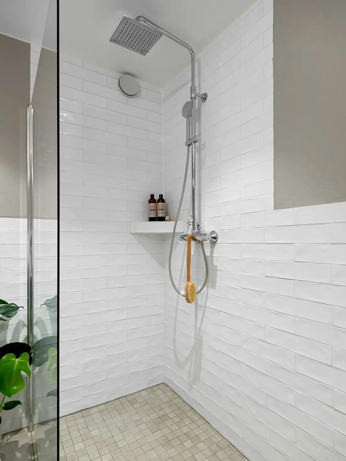 Walk-in shower with white wall tile and a glass door